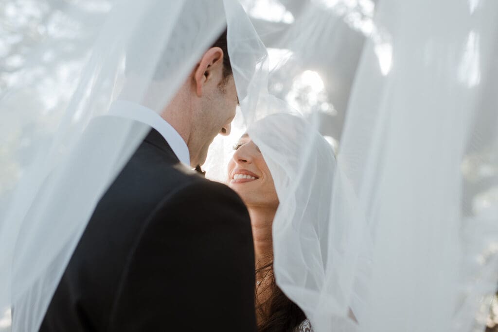 Bride and groom laughing together under vail.